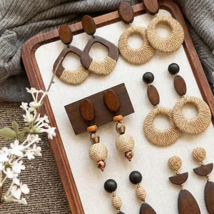 Close-up detail showing assorted bohemian raffia woven and wooden earrings on a wooden tray
