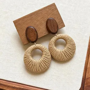 Detail of bohemian hand-woven raffia circular earrings with wooden oval studs.
