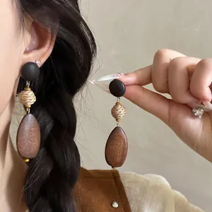 Detail shot of bohemian raffia woven and dark wooden drop earrings worn by a model.