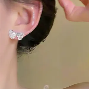 Detail shot of delicate beaded bow stud earrings worn on ear in elegant Korean style