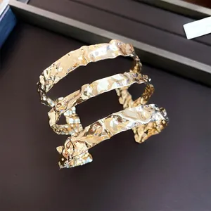 Vista detallada de un brazalete dorado de tres capas en metal con textura martillada.