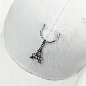Dettaglio ravvicinato di un cappellino bianco con ciondolo Torre Eiffel e anello metallo