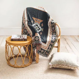 Bohemian woven throw blanket with fringe and geometric patterns draped on a rattan chair