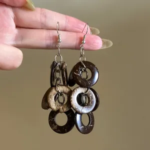 Ethnic style earrings with dark brown circular wood pendants held by hand.