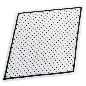 Détail d'un foulard carré en satin blanc avec motif à pois noirs et bordure contrastée.