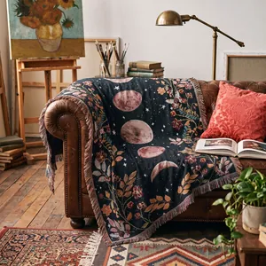 Bohemian woven throw blanket with moon and floral patterns draped over a leather sofa.