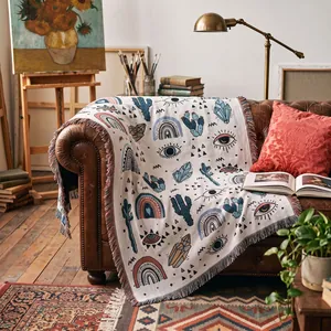 Bohemian woven throw blanket with mystical eye and cactus patterns on a vintage sofa.