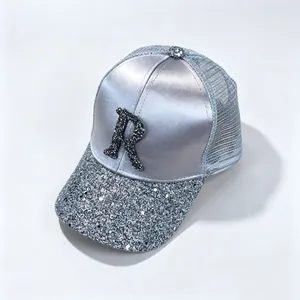 Close-up of silver satin baseball cap with rhinestone letter R and sequined brim