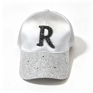 Close-up of a silver satin baseball cap with rhinestone letter R and glitter brim