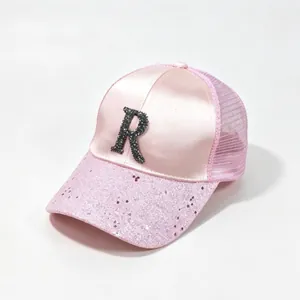Close-up of pink satin trucker hat with a rhinestone R letter and sequined brim.