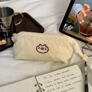 Close-up of a cream canvas pencil case with a cute cat embroidery in a cozy desk setting.