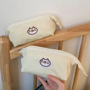 Close-up view of a minimalist cream canvas pencil case featuring a cute embroidered cat logo