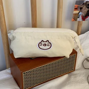 Close-up detail of a cute embroidered cat patch on a minimalist cream canvas pencil case