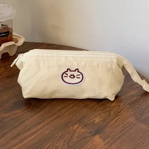 Close-up detail of a cream canvas pencil case featuring a cute embroidered cat mascot