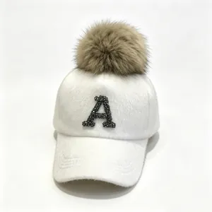 Close-up of white furry baseball cap with rhinestone letter A and brown fur pom-pom detail.
