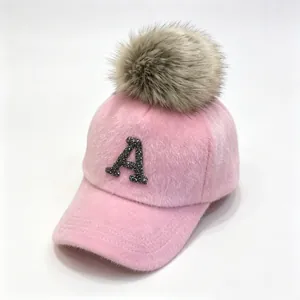 Close-up of pink furry baseball cap featuring a rhinestone letter A and a fluffy pom-pom.
