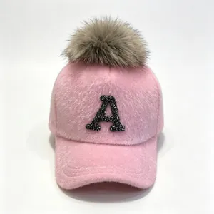 Close-up of pink faux fur baseball cap with rhinestone letter A and fluffy pom-pom.