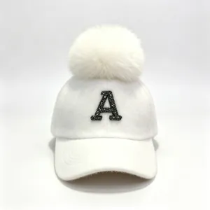 Detailed shot of a white winter baseball cap featuring a rhinestone letter A and a fluffy pom-pom