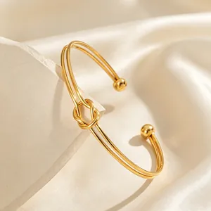 Dettaglio di un bracciale rigido aperto in acciaio inossidabile dorato con nodo centrale.