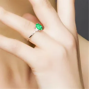 Detailaufnahme eines ovalen Rings mit grünem Edelstein und Diamantakzenten an der Hand.