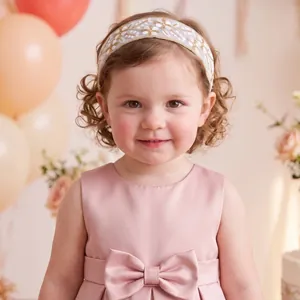 Detailed view of a toddler girl wearing a white floral lace headband with gold embroidery