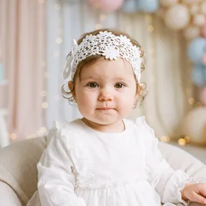 Close-up view of a baby girl wearing a white lace floral headband with a ribbon bow accessory