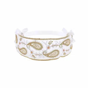 Detail of white lace headband for babies with gold paisley embroidery and satin bows.