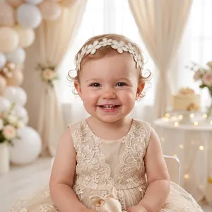 Gros plan d'un bébé souriant avec un bandeau de fleurs en dentelle ivoire et perles.