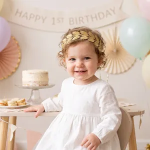 Détail d'un bébé portant un bandeau avec des feuilles brodées dorées pour son 1er anniversaire