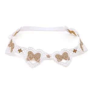 Gros plan d'un bandeau en dentelle blanche pour bébé avec un joli nœud brodé doré.