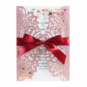 Pink glitter laser-cut wedding invitation card with red ribbon bow and floral detail