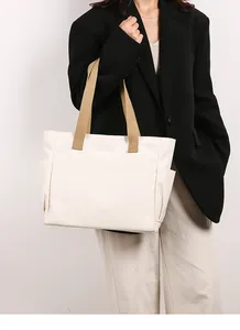 Close-up of a large white canvas tote bag with khaki straps worn by a model