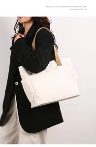 Close-up detail of a large white canvas tote bag with khaki straps on a model
