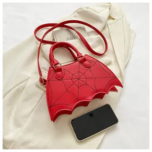 Esclusiva borsa rossa a forma di pipistrello con cuciture a ragnatela accanto a uno smartphone.