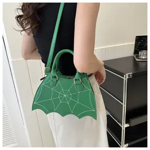 Dettaglio di una borsa a mano verde a forma di pipistrello con ricamo a ragnatela bianca.