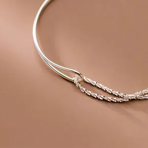 Detail view of an asymmetric silver bracelet with a curved tube and double starry chain.