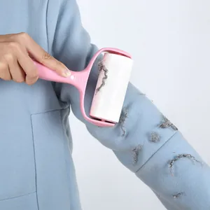 Pink handheld lint roller removing fuzz from a light blue wool coat sleeve