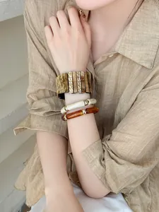 Gros plan de bracelets superposés en acrylique iridescent et ambre au poignet du modèle