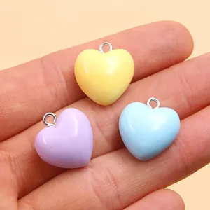 Close-up of colorful 17x18mm resin heart pendants held in palm for DIY jewelry making.