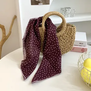 Nahaufnahme eines burgunderfarbenen gepunkteten Seidenschals an einer Strohtasche