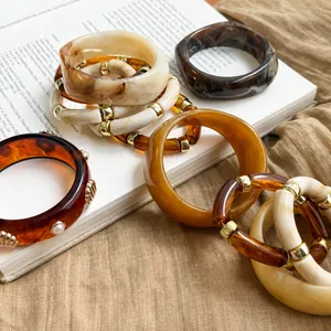 Vue détaillée de divers bracelets en acrylique écaille et crème disposés sur un livre ouvert.