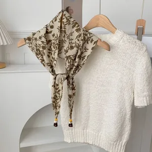 Detail eines quadratischen Seidenschals mit Blattmuster und Perlen auf weißem Pullover