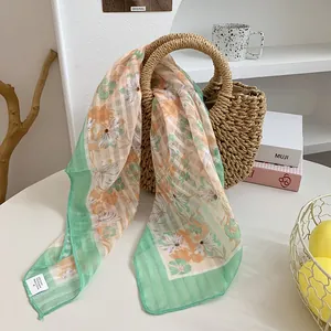 Detailansicht eines weichen Satin-Halstuchs mit Blumendruck auf einer Strohtasche