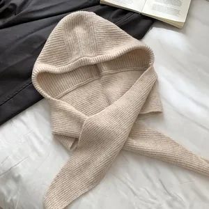 Nahaufnahme eines beige gestrickten Kapuzenschals mit Rippenstruktur auf weißem Bettzeug