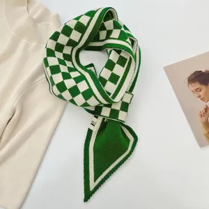 Detailansicht eines modischen grün-weiß karierten Strickschals auf einer weißen Oberfläche