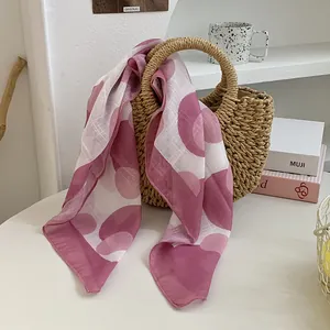Detail eines rosa-weiß gemusterten Seidenschals, der über eine Korbtasche drapiert ist.