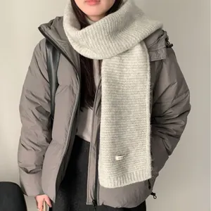 Detail eines gemütlichen hellgrauen Strickschals aus Wollmischung mit einer grauen Daunenjacke