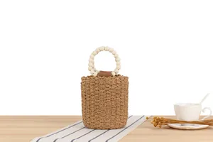 Handgefertigte runde Stroh-Eimertasche mit einem dekorativen Griff aus weißen Holzperlen