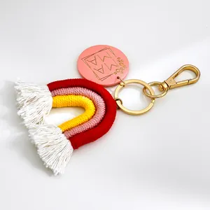 Handgemaakte macramé regenboog sleutelhanger met MAMA houten schijf en witte kwastjes.