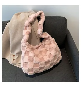 A detailed view of a soft pink plush checkered tote bag displayed on a grey sofa.